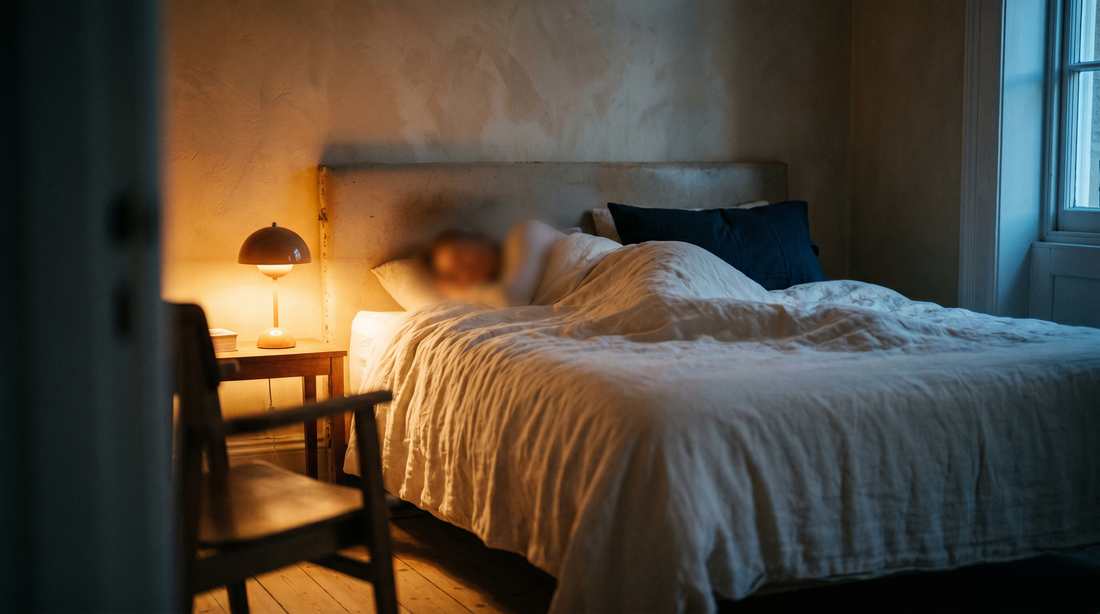 A peaceful sleeping figure under cream linen duvet with soft warm bedside lamp glow