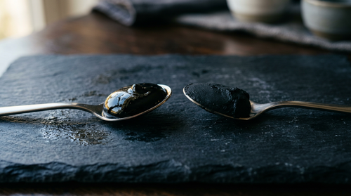Two spoons comparing genuine glossy shilajit resin with a dull imitation