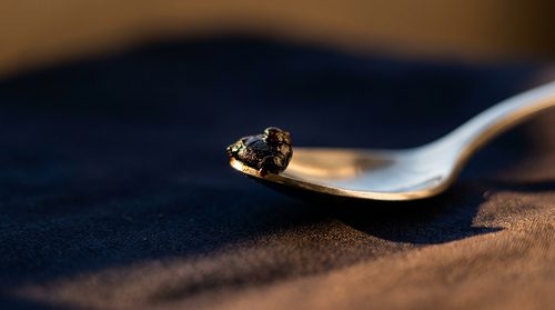 Rice grain sized portion of shilajit resin on a spoon showing a single dose